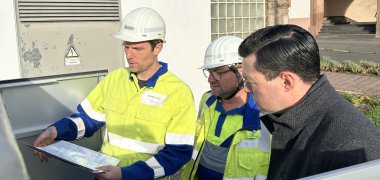 Projektingenieur und Netzplaner erklären Bürgermeister Dr. Johannes Reuschen wie eine digitale Ortsnetzstation im Fall einer Störung hilft, Ausfallzeiten zu reduzieren. Hierfür stehen sie mit Plänen vor der Ortsnetzstation