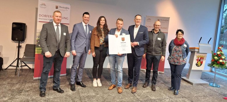 Gruppenfoto mit mehreren Personen bei der Übergabe der Urkunde: Vertreter der Ortsgemeinde Auw bei Prüm und der Verbandsgemeinde Prüm halten gemeinsam die Auszeichnung zur Anerkennung als Schwerpunktgemeinde.