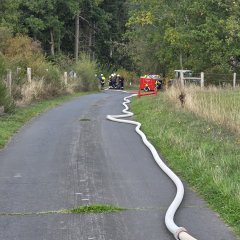 wasserbefüllter Schlauch, der zu einem Feuerwehrauto zur Förderung des Wassers liegt.