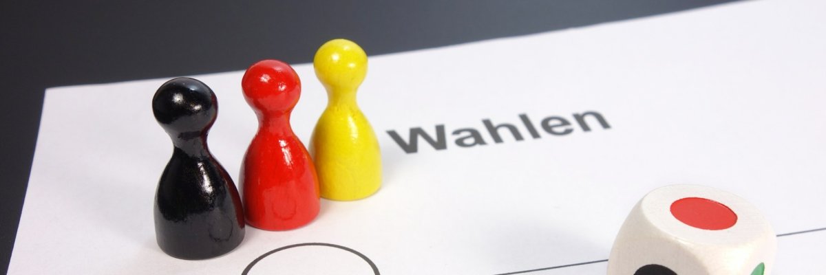 Drei Spielfiguren in Schwarz, Rot, Gelb auf Wahlzettel