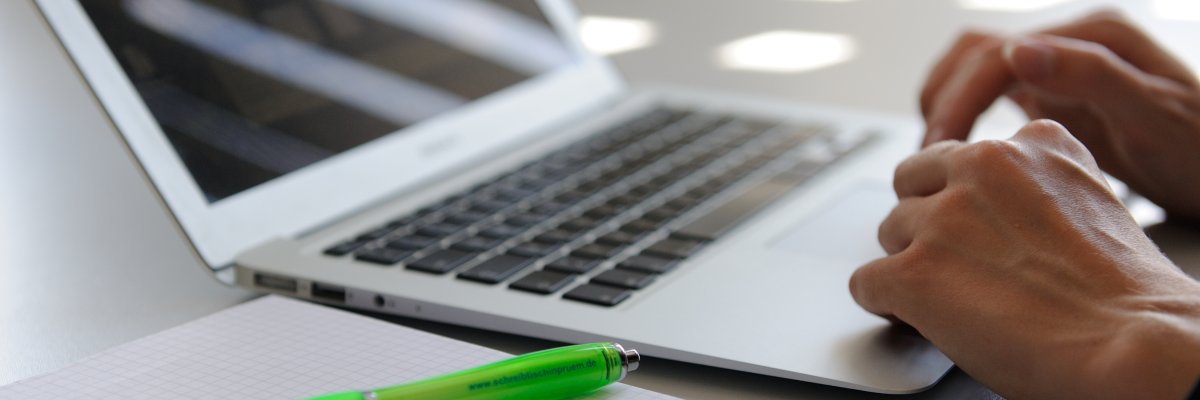 Laptop mit Händen, die etwas schreiben